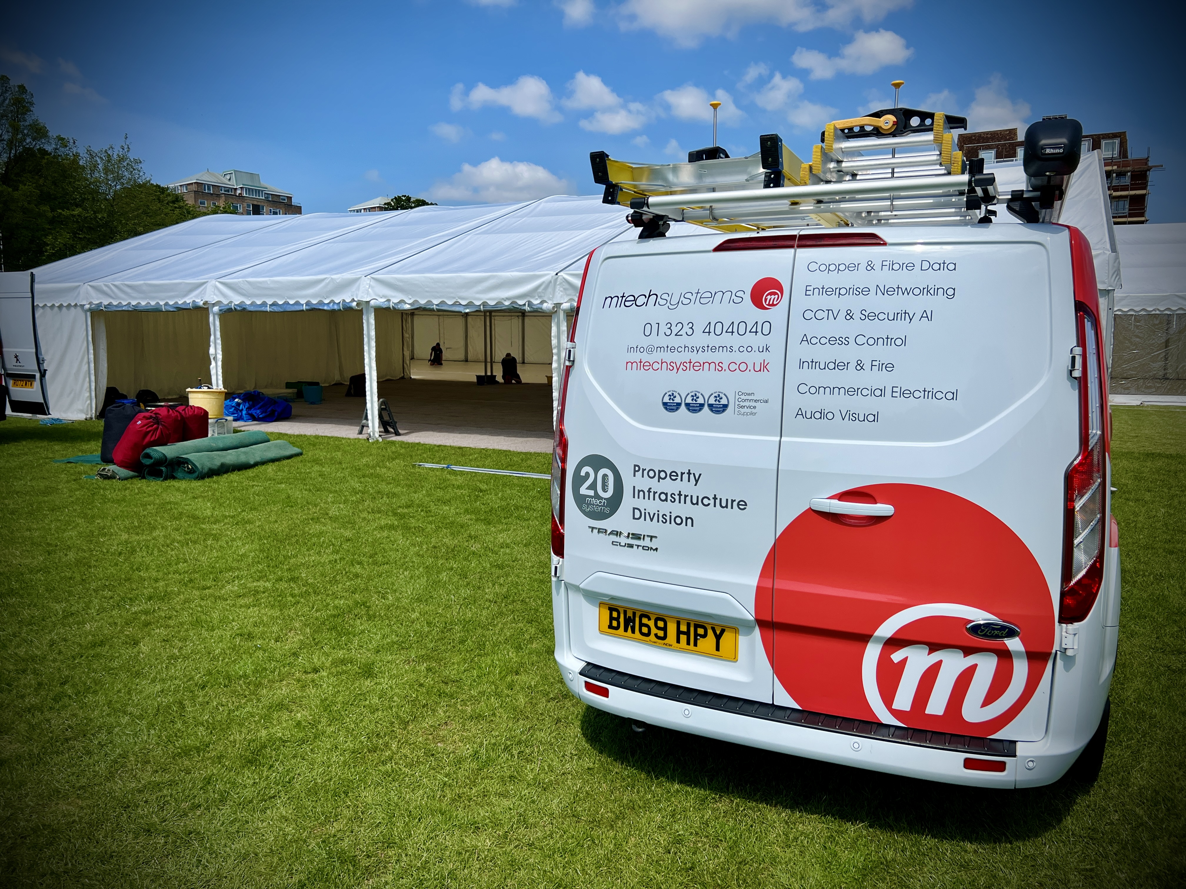 M-Tech-branded service van parked beside the Chiddfest marquee on build day, ladders on the roof