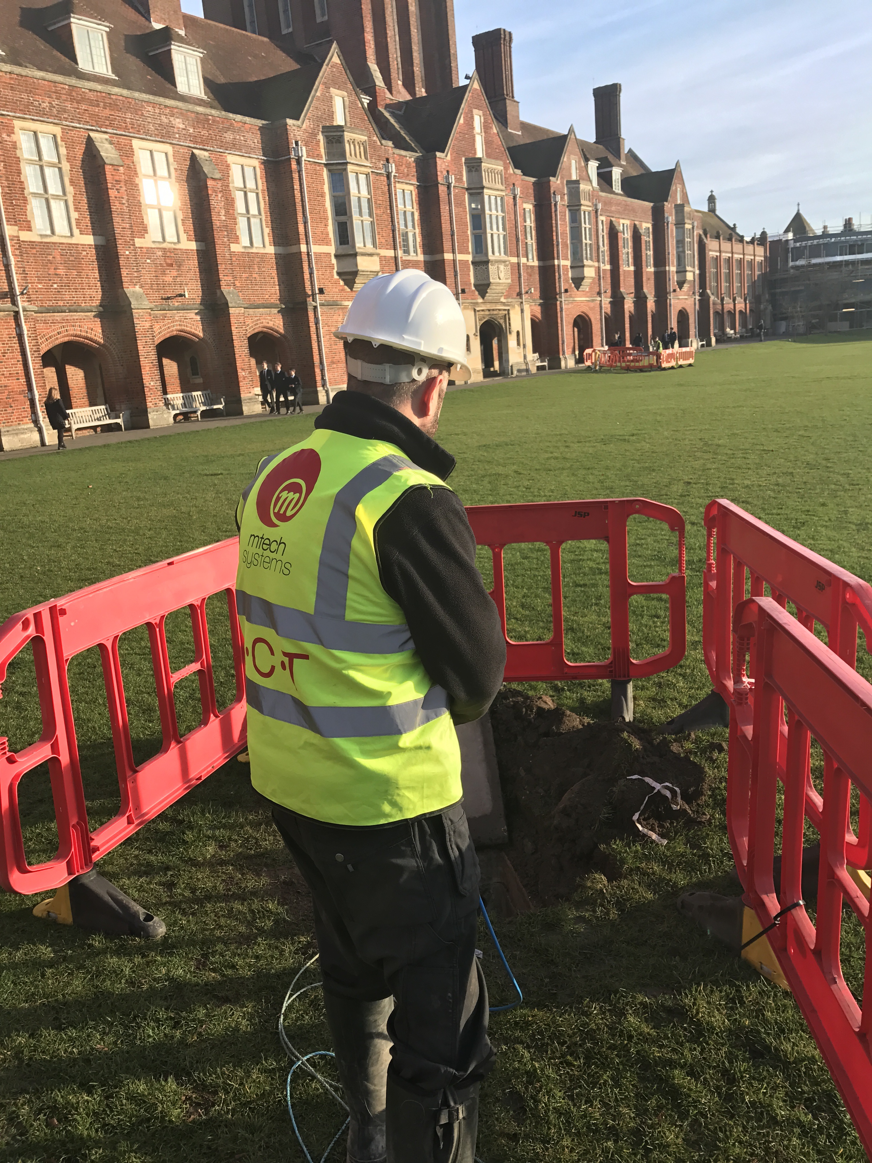 M-Tech engineer in PPE on the lawn at Eastbourne College, working inside red trench guards as fibre is laid back to the comms room