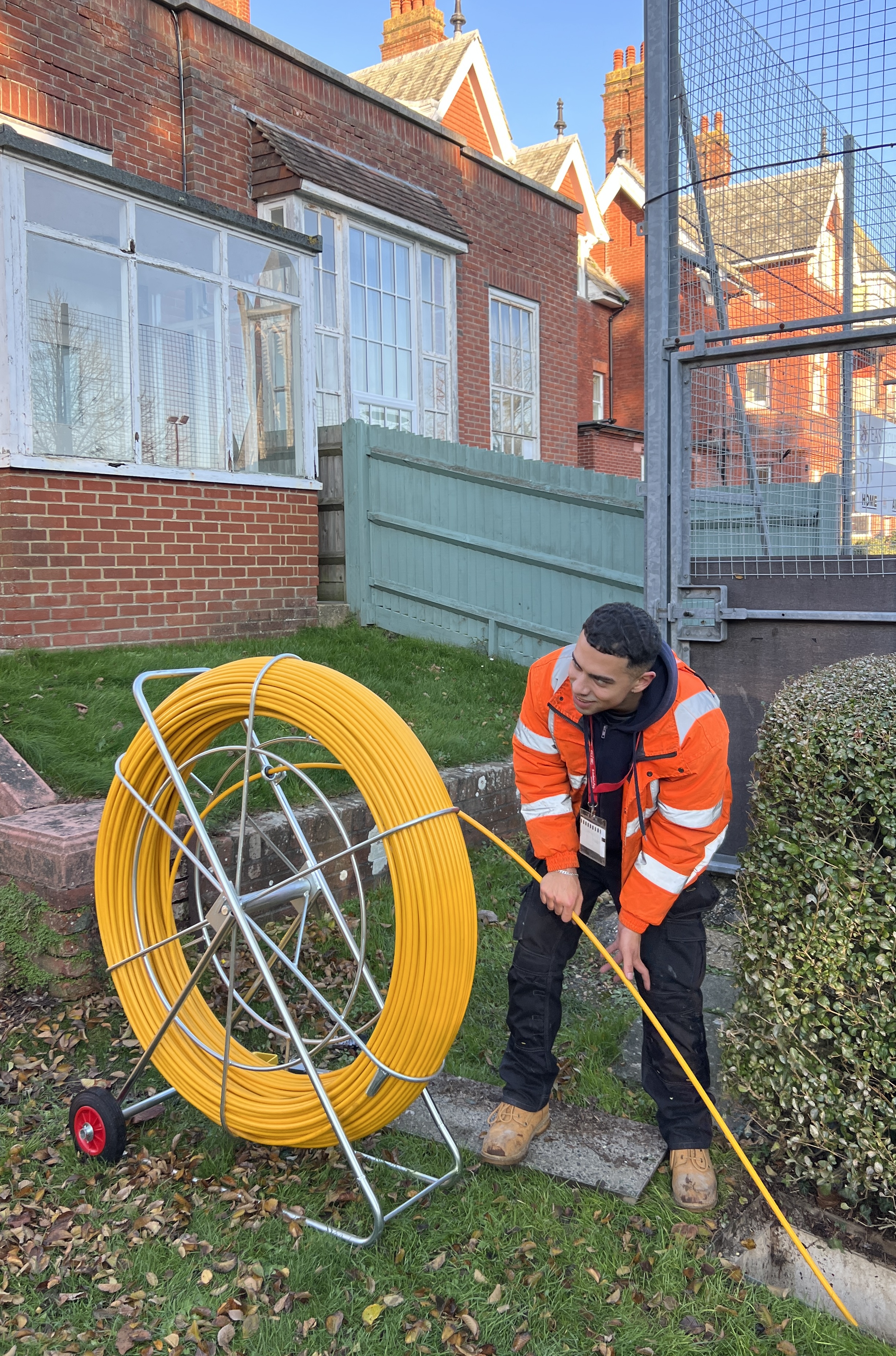 M-Tech engineer pulling a fibre run through underground duct at Eastbourne College, with a large duct-rod reel beside him